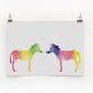 A digital print featuring two zebras in a rainbow color stripe pattern, mounted on a wall.