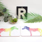 A set of placemats featuring a rainbow-colored zebra design, displayed on a table with a plant, a coaster, and a fork.