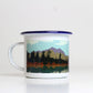 A white enamel mug with a blue lid, featuring a printed design with a mountain and pine forest landscape.