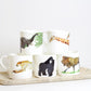 A set of bone china mugs with various animal designs, including a lion, gorilla, elephant, two giraffes, and a cheetah, displayed on a wooden tray against a white background.