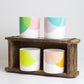 A set of bone china mugs with various color combinations displayed in a wooden crate.