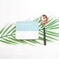 A blue and white geometric patterned coaster with a decorative element presented on a green palm leaf background.
