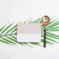 A square coaster with a geometric pattern, placed on a white surface alongside a spoon and a leaf.