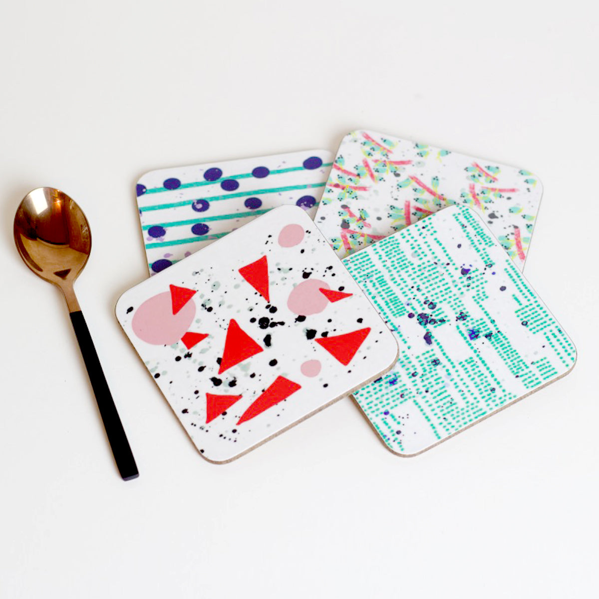 A set of four square coasters with various sound-inspired patterns including dots, lines, and geometric shapes, displayed on a white background alongside a teaspoon for scale.