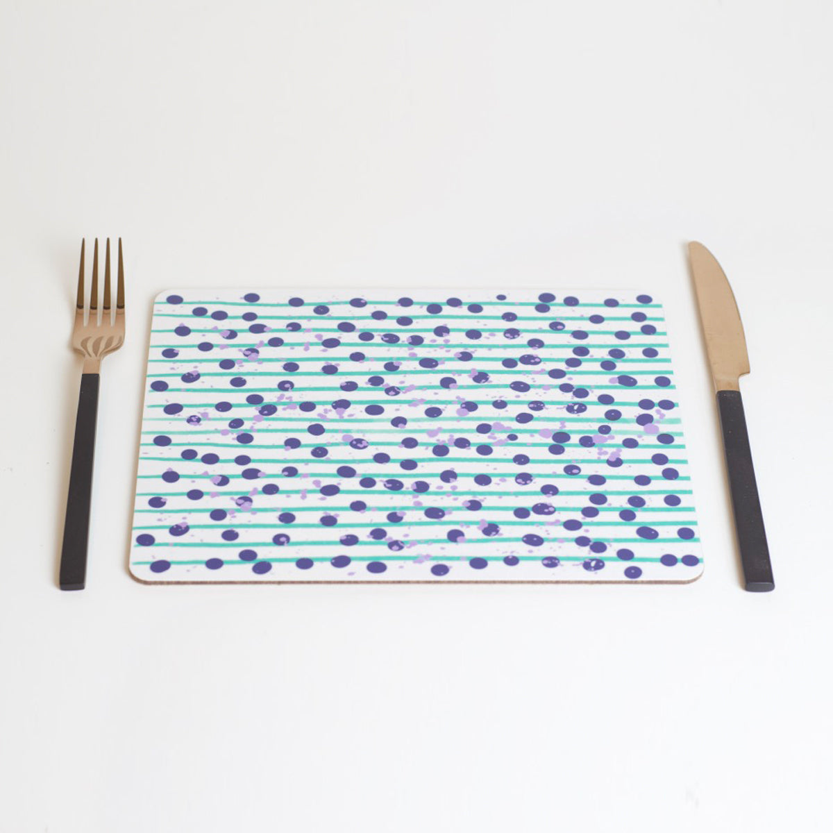 A rectangular placemat with a green and blue dot pattern, featuring a fork on the left side and a knife on the right side, placed on a white background.