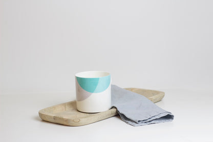 A two-tone bone china mug with a teal and grey design, placed on a wooden board next to a grey napkin.