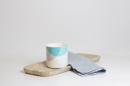 A two-tone bone china mug with a teal and grey design, placed on a wooden board next to a grey napkin.