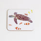 A square coaster with a cork backing, featuring a hand-drawn design of a turtle and multiple clown fish.