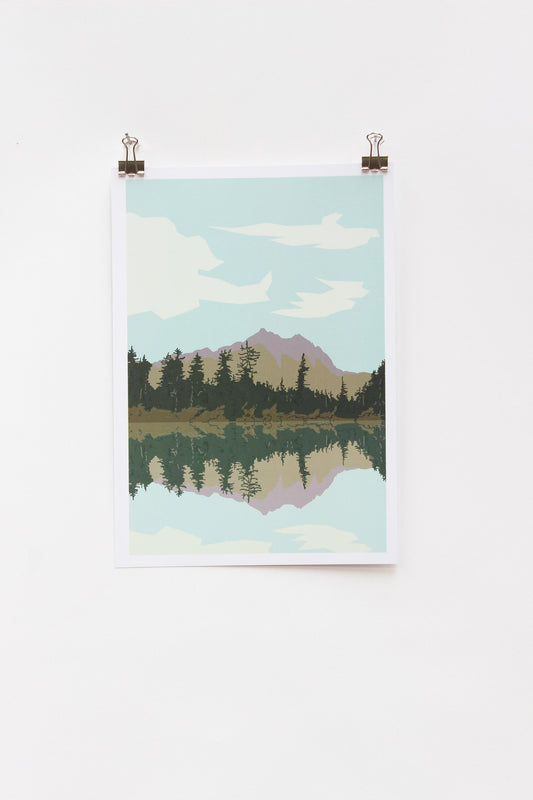 A digital print of a lake scene with mountains in the background, hanging on a wall with two clip bookmarks on the sides.
