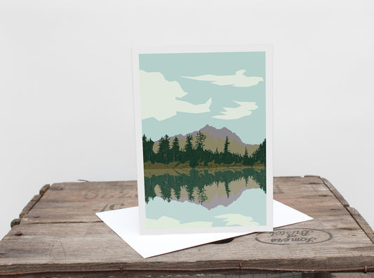 A greetings card with a landscape image of a lake and mountains on it, placed on a wooden surface.