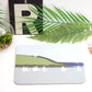 A placemat with a boat design, laid out on a table with cutlery and a plant in the background.