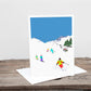 A greetings card with a winter skiing scene, featuring mountains, skiers, and trees on a blue background.