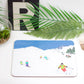 A placemat with a ski-themed design, featuring skiers on a snowy mountain, placed on a dining table with cutlery and a plant in the background.