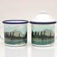 Two enamel mugs with lids, featuring a hand-illustrated design of a lake and forest scene.