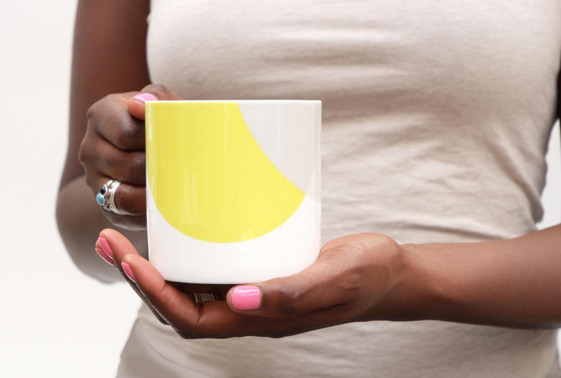 A person holding a bone china mug with a yellow design on a grey background.