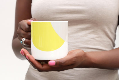A person holding a bone china mug with a yellow design on a grey background.