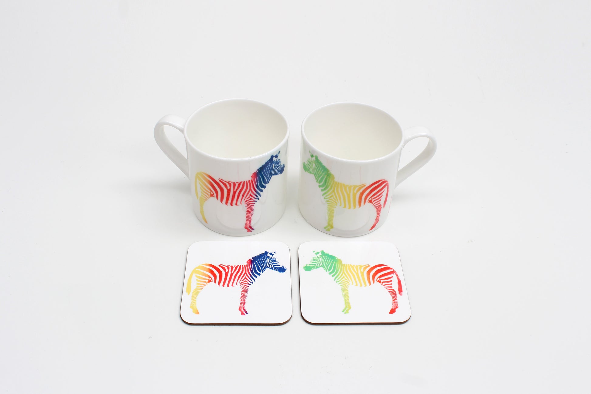 Two square coasters with a multicolored zebra pattern on a white background, displayed on a white surface.